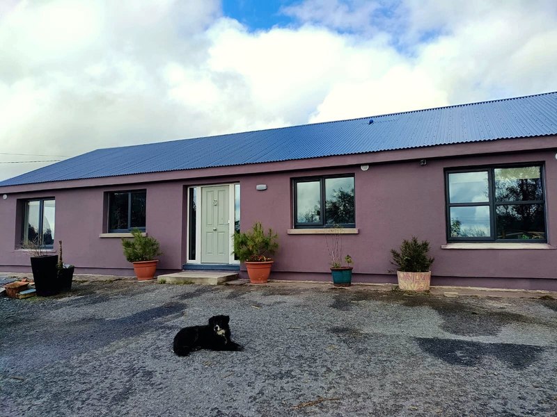 Long single-storey bungalow with freshly rendered plum walls and a new grey front door