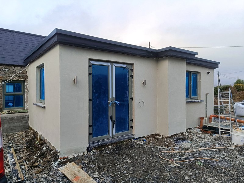 New flat-roof extension with cream render and grey French doors on a stone cottage
