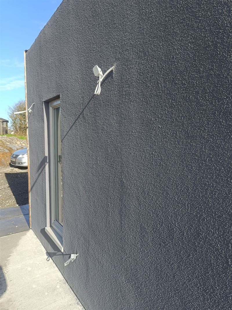 Finished grey textured render on the side wall of a house, beside a door