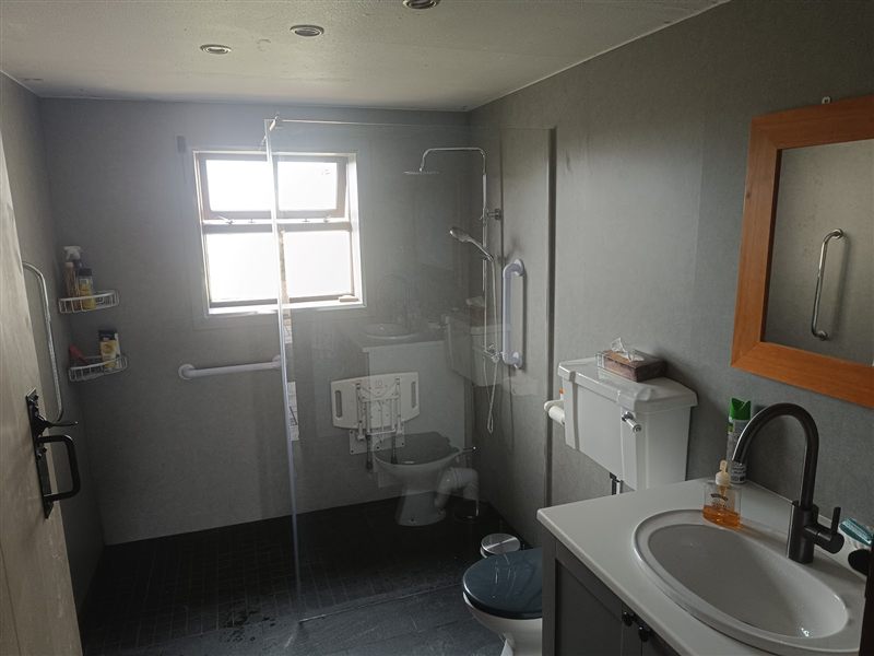 Accessible wet room with grey wall panels, glass screen, grab rails and a fold-down shower seat
